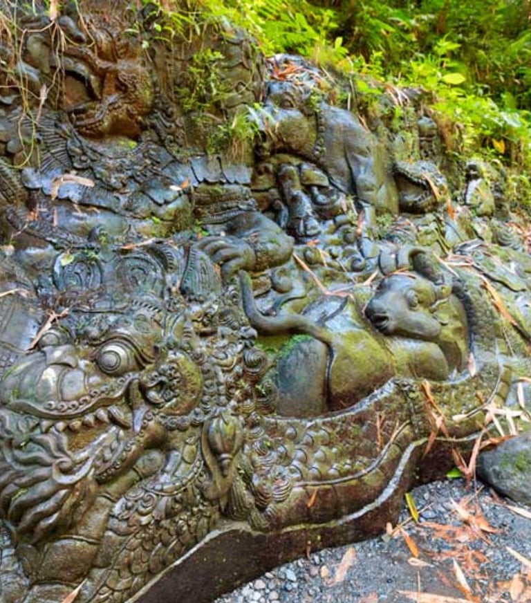 Ancient Balinese stone carvings of mythical creatures and dragons on a mossy jungle wall.