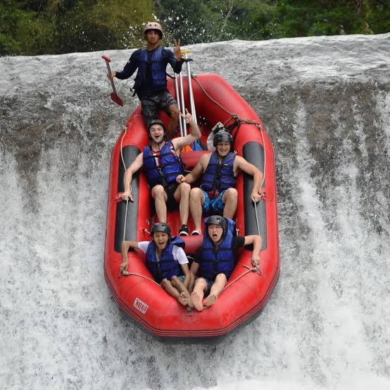 Excited group of tourists on a white water rafting adventure descending a waterfall in a red inflatable boat.