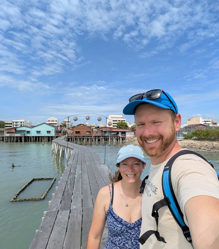 A smiling couple taking a selfie on a wooden pier over the water with stilt houses in the background