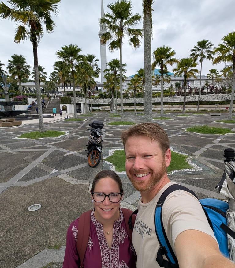  Don and Samantha take selfie at the National Mosque of Malaysia with palm trees and a minaret.