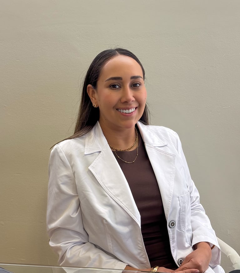 Smiling female medical professional in a white lab coat sitting at a desk.