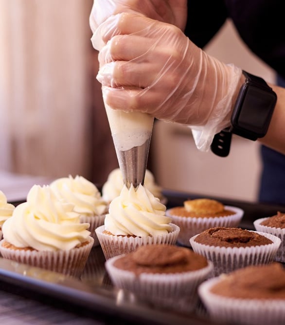 Photo of person piping icing onto a tray of cupcakes