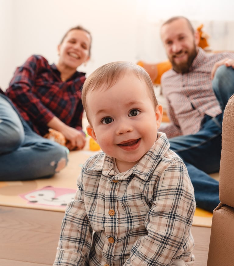 mala beba, iza nje sjede nasmiješeni roditelji
