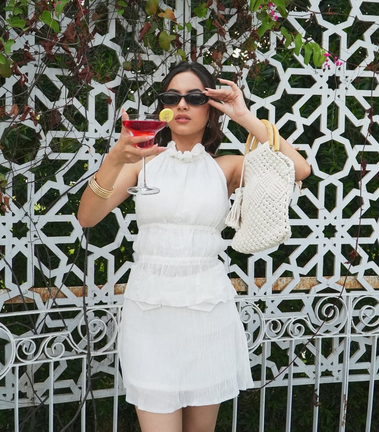 Woman in white summer dress holding a red cocktail and a woven handbag.