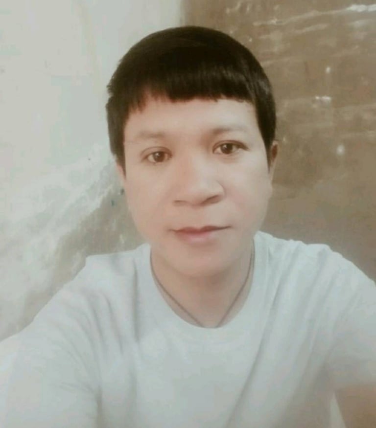 Male massage therapist wearing a light shirt, looking at the camera indoors with a calm expression and soft lighting.