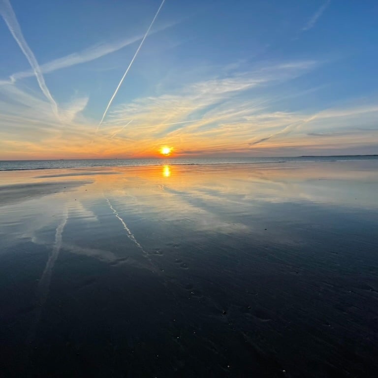 a sunset on a beach with a plane flying over the water