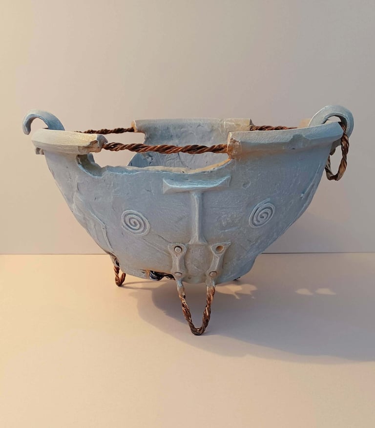 A fragmented, round bowl-like sculpture adorned with symbols and letters, finished in blue-grey hues