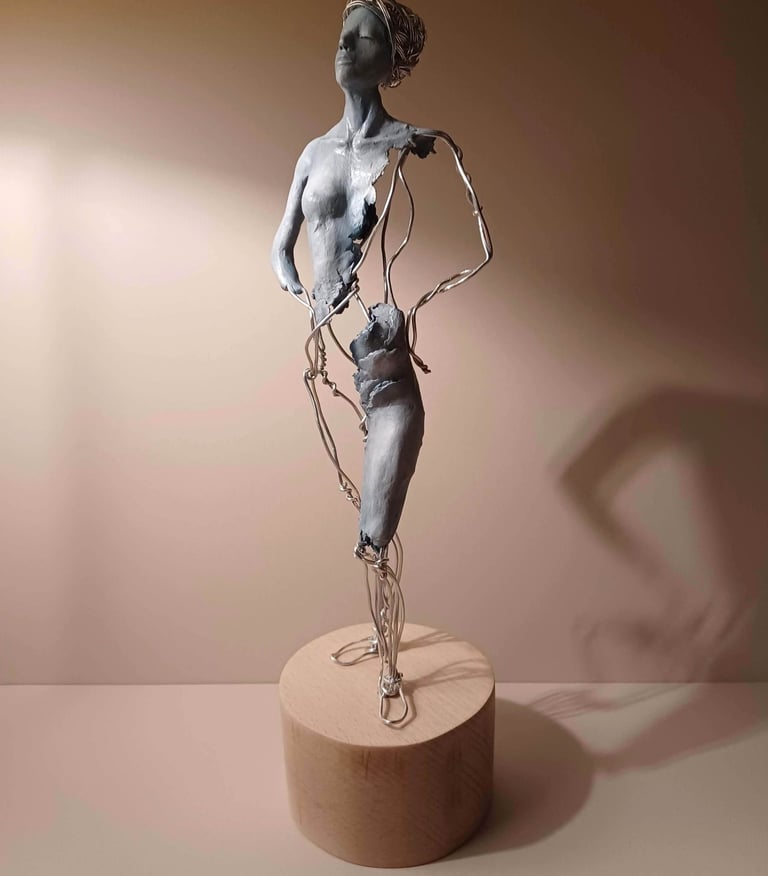 A complete sculpture of a standing female figure, part clay, part wire, hands on hips