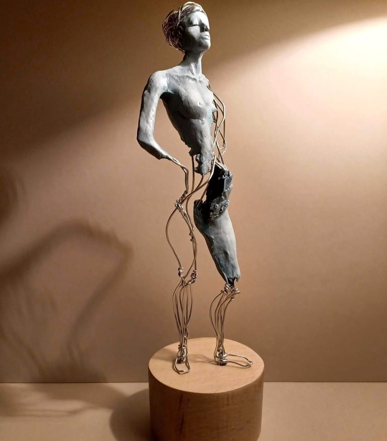 A complete sculpture of a standing female figure, part clay, part wire, hands on hips