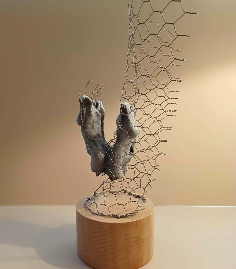 A sculpture of two female torsos, back to back, surrounded by wire netting, painted blue-greys