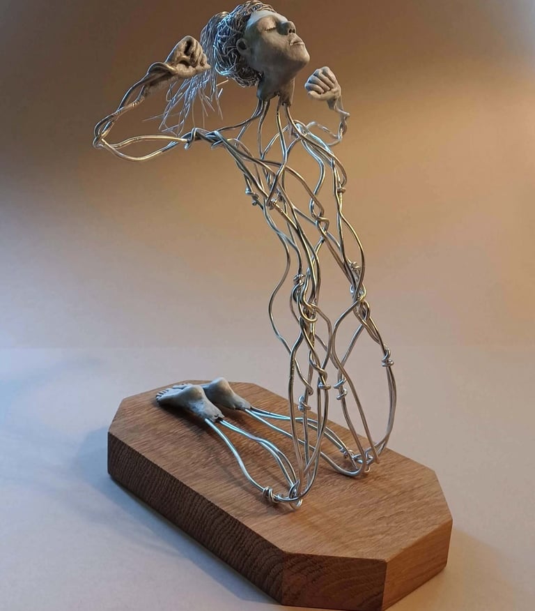 A wire sculpture of a complete kneeling female figure with clay hands, face and feet, arms raised