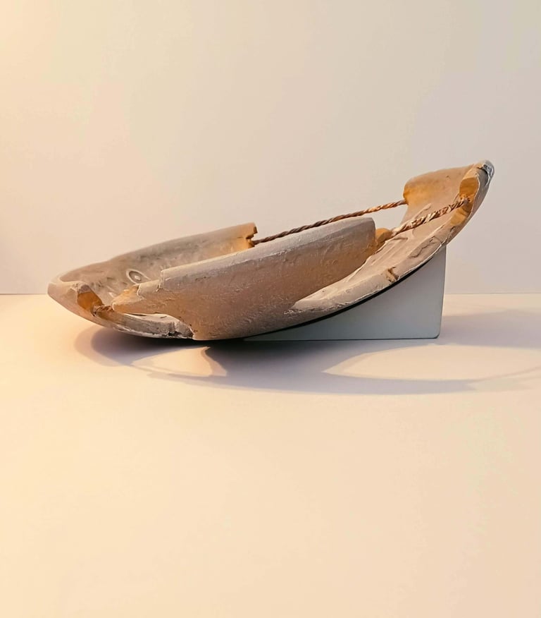 Side view of a bowl-like sculpture with embossed horse figures and symbols in rust/brown hues