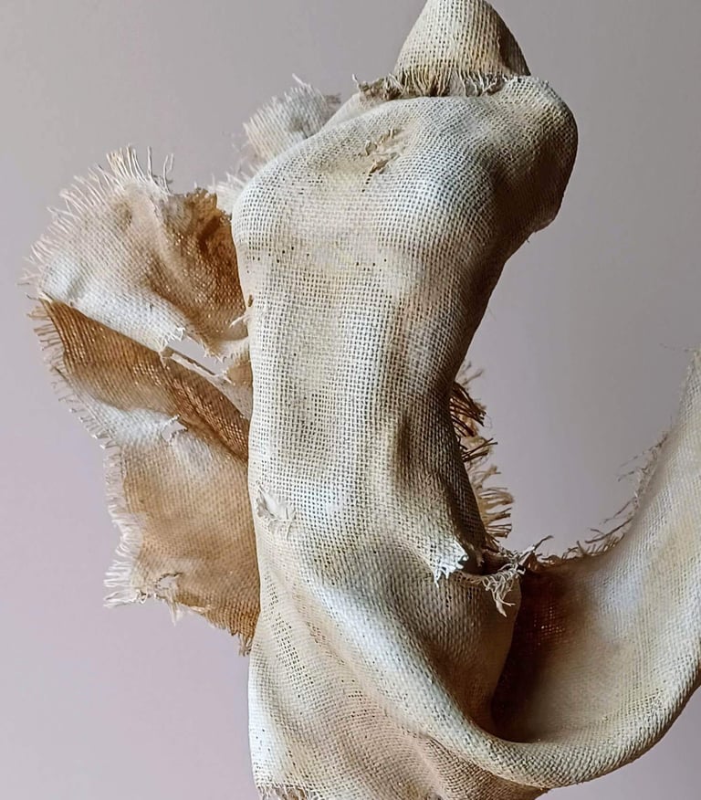 Close up image showing a clay and canvas sculpture of a female torso with windswept, ragged clothes.