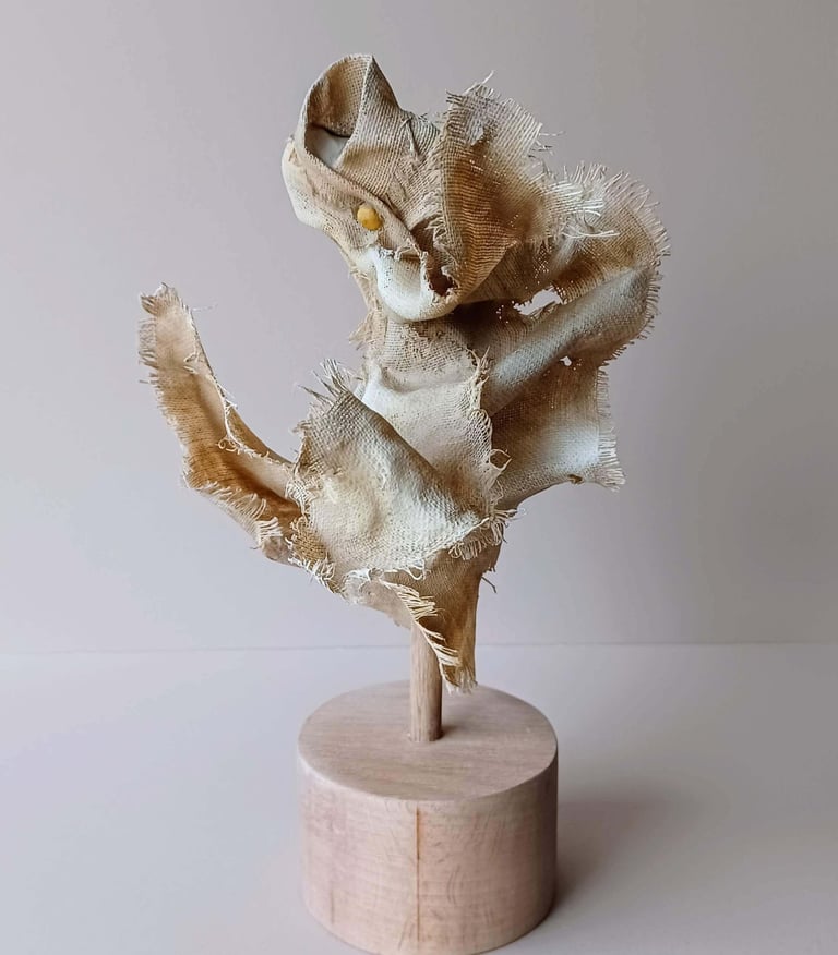 Rear view, showing a clay and canvas sculpture of a female torso, with windswept, ragged clothes.