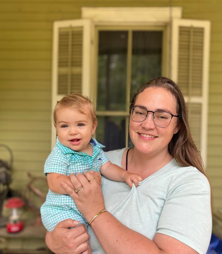 a woman in glasses and a blue shirt holding a baby