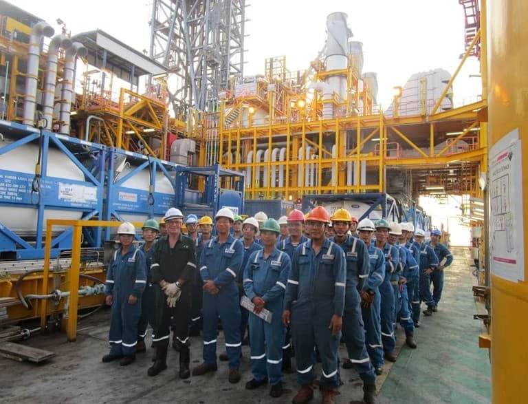 A group of industrial engineers and workers in blue jumpsuits posing at an offshore oil and gas platform.