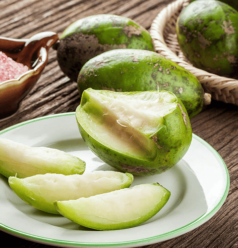 Slices of fresh June Plum fruit served on a white plate with pink salt.