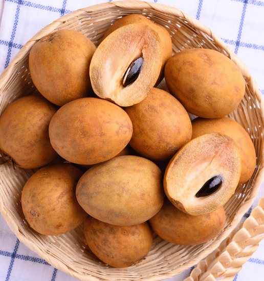Fresh ripe sapodilla fruit and sliced chikoo with seeds in a wicker basket.
