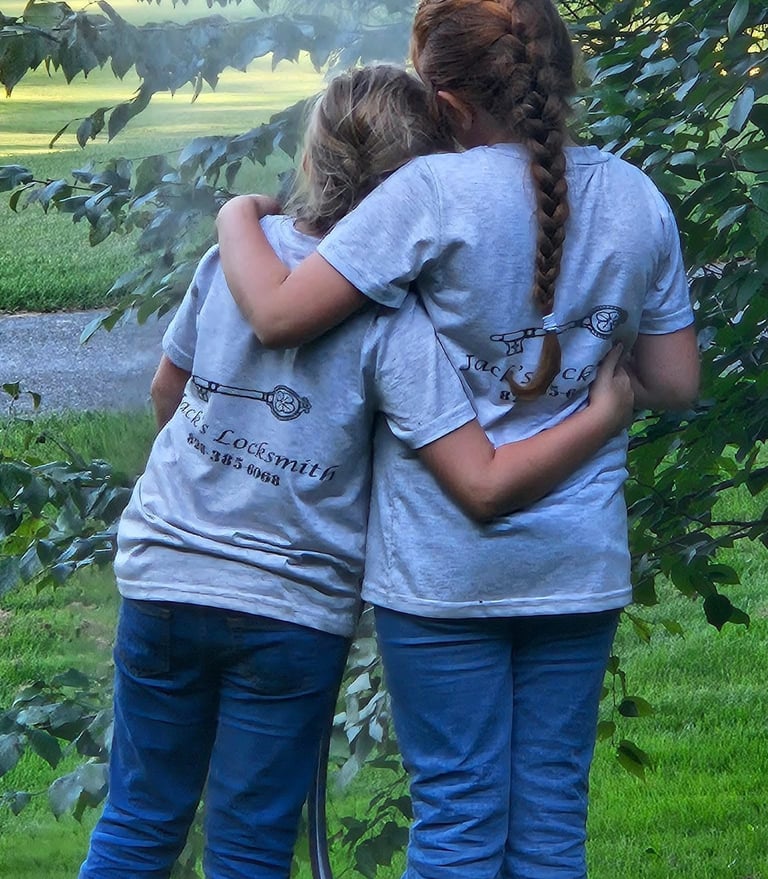 Two daughters hugging outdoors while wearing matching locksmith work shirts