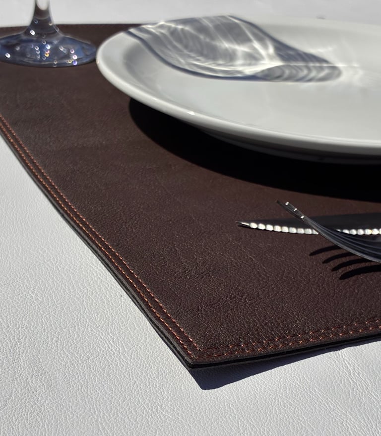 Foto detalle de una esquina de un individual de similcuero, ambientado con plato, copa y cubiertos
