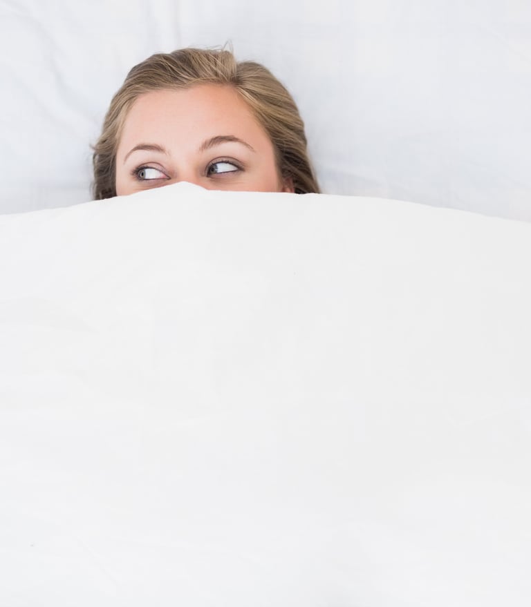 a woman is peeking behind a blanket in a bed