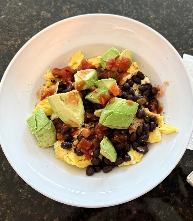 Scrambled eggs with black beans, avocado, and salsa in a white bowl.