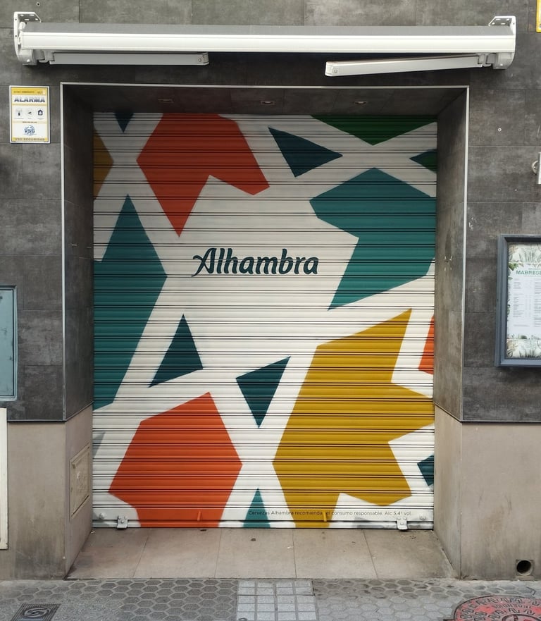 Graffiti corporativo Cervezas Alhambra en cierre metálico de restaurante MadreSelva en Sevilla