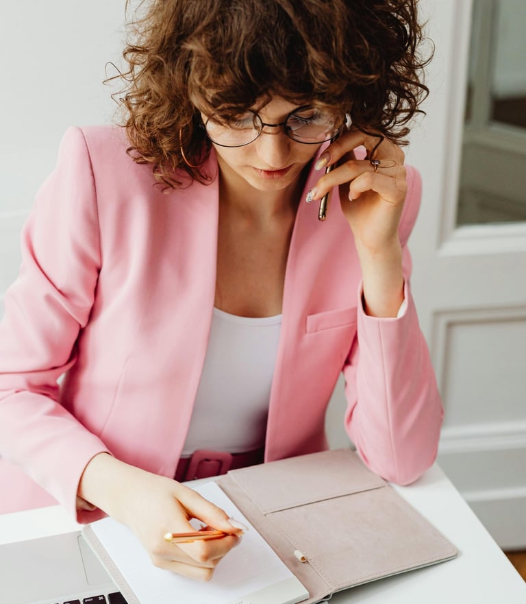 A laptop and open notebook on a desk with a female taking notes.