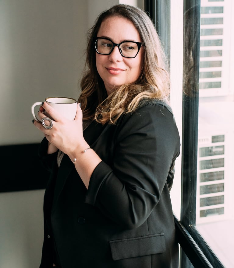 Uma mulher profissional vestindo um blazer preto, segurando uma caneca de café perto de uma janela i