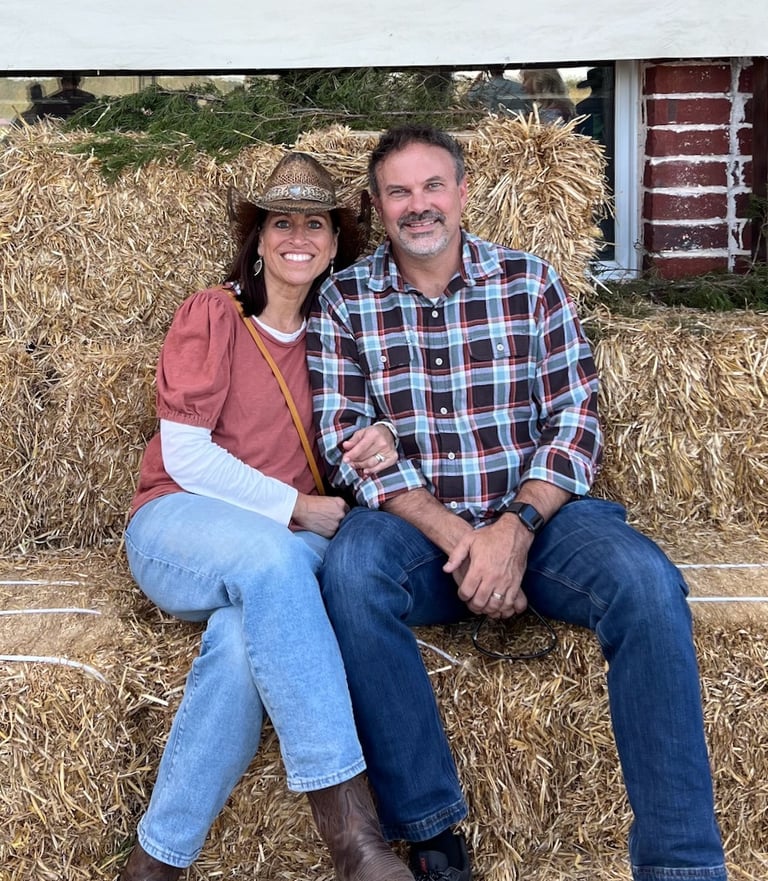 Monica Weaver and her husband smiling and sitting on bales of hay