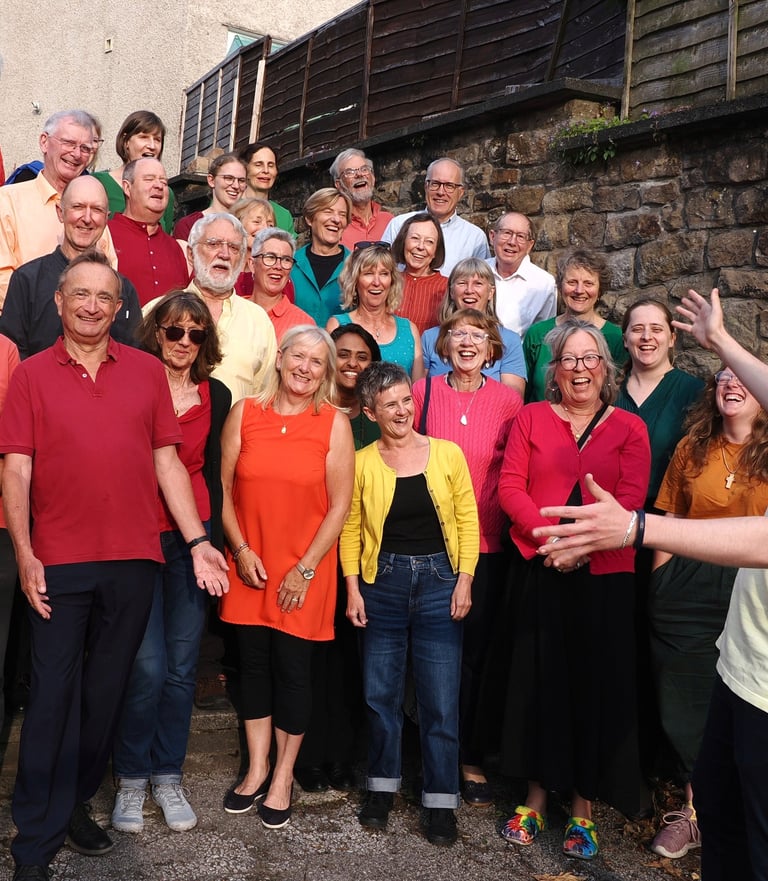 The choir singing outside wearing bright coloured tops