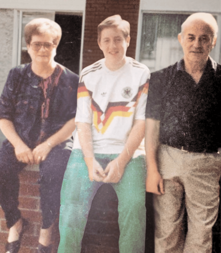 Vintage family photo of a boy in a German soccer jersey sitting with his grandparents outside.