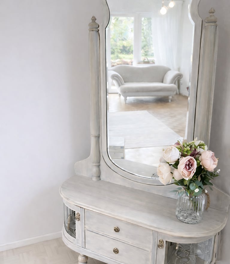 Vintage grey wooden vanity table with large mirror and bouquet of pink roses in a bedroom.