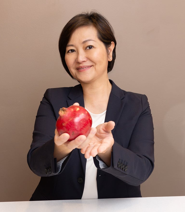 a woman in a dark suit holding a red pomegranate in her hand