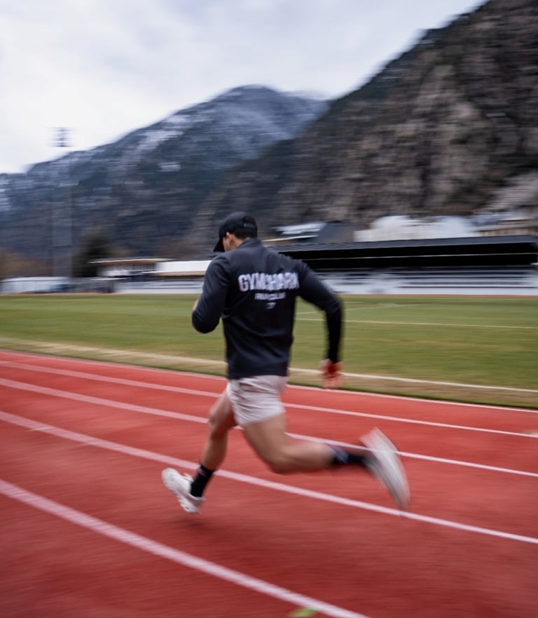 Male athlete in Gymshark apparel sprinting on a red outdoor track with mountains in the background.