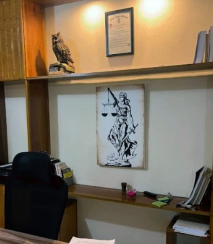 Pared blanca de oficina con repisas. Un diploma, un cuadro decorativo alusivo a la justicia y un buho