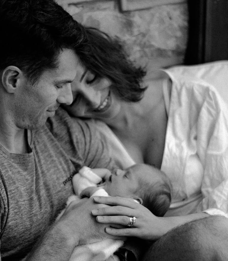 a newborn in her mom & dads arms, looking down at her in a lifestyle newborn shoot