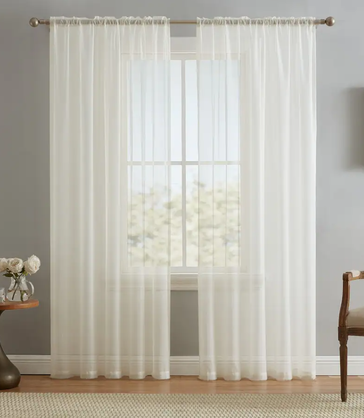 Elegant sheer white curtains hanging on a bronze rod over a window in a gray room.