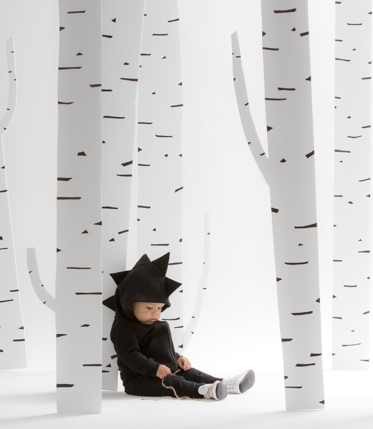 Fashion campaign photography - a baby in a black dinosaur outfit sitting by trees