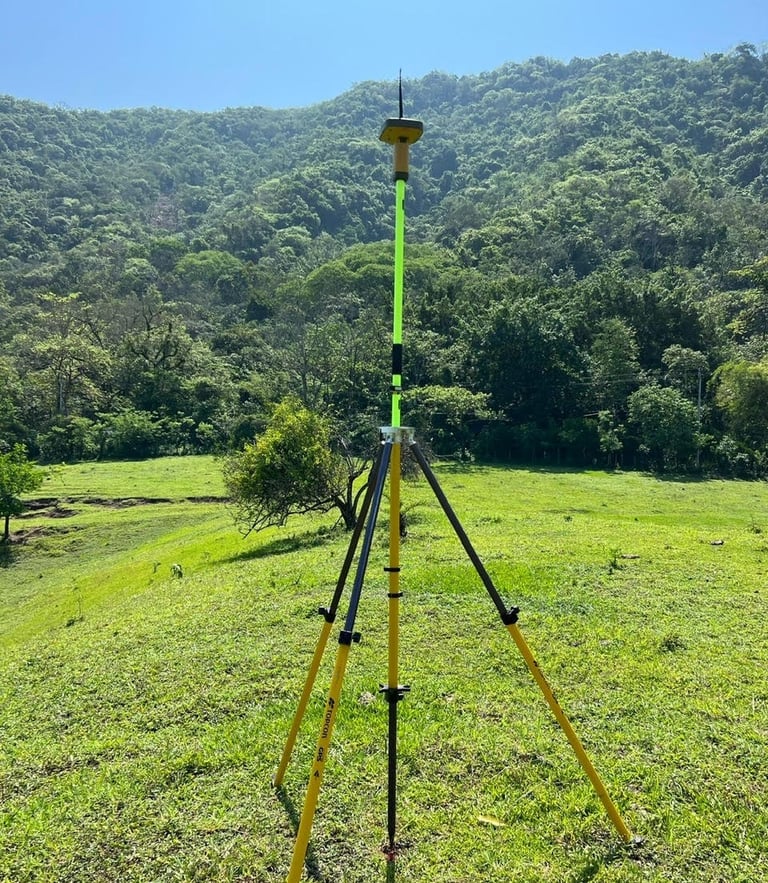 Professional GPS surveying equipment on a tripod in a grassy field with lush green mountains.