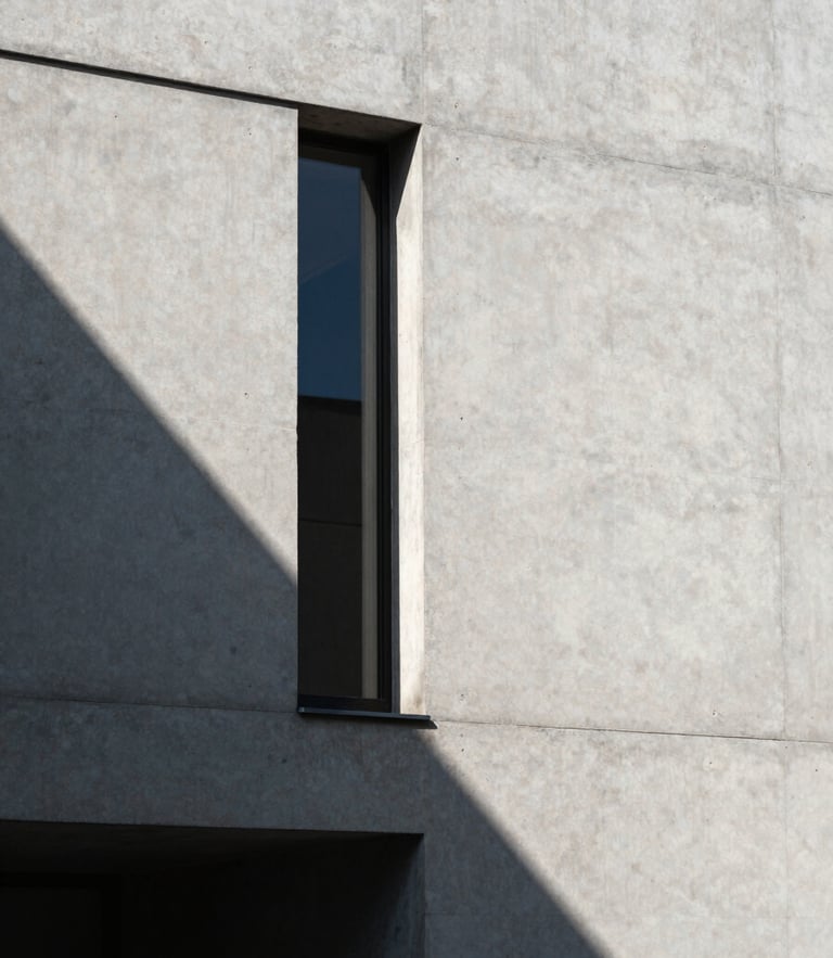 Sharp architectural detail of a concrete minimalist building facade, casting a stark geometric shadow under direct sunlight.