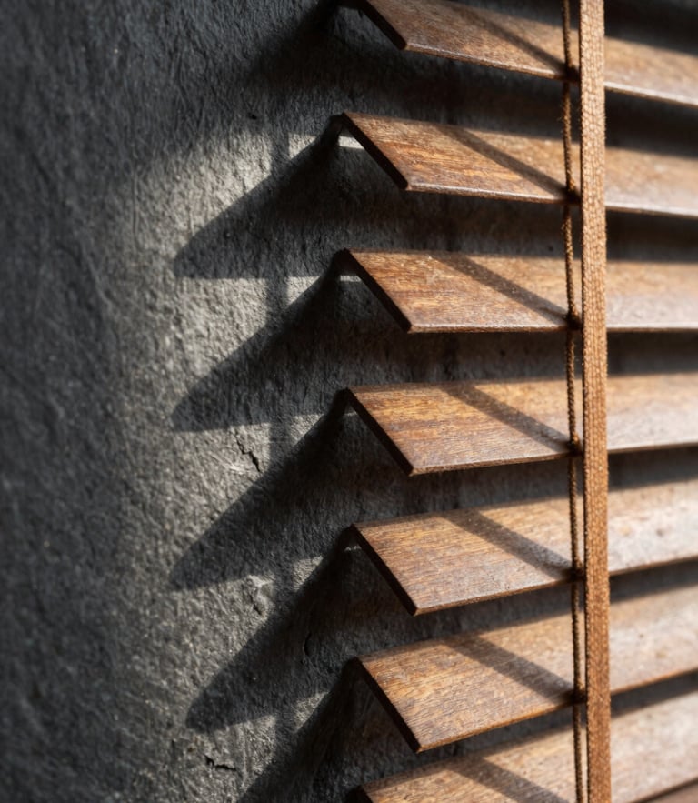 Macro close-up of warm afternoon light filtering through wooden blinds onto a dark slate wall, casting long architectural shadows, quiet library atmosphere.