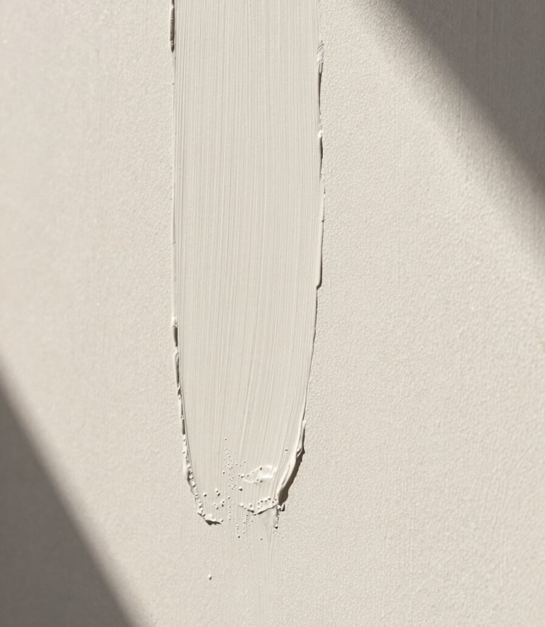 Extreme close-up of a hand-applied lime wash wall texture, warm chalky white color, soft natural side light casting delicate shadows, architectural minimalism.