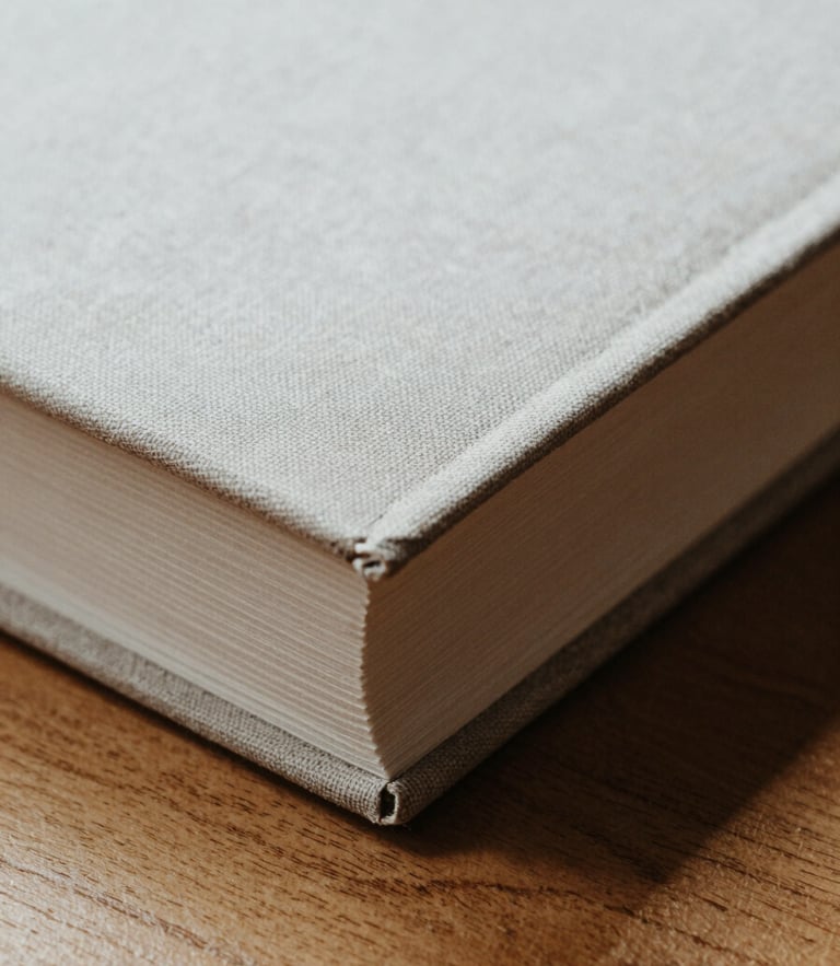 Macro close-up of a heavy linen book cover open on a solid oak table, soft north-facing daylight casting deep shadows