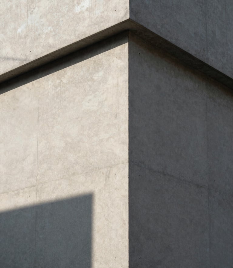 Stark architectural corner of a concrete building, sharp geometric shadow cast by midday sun on a textured wall, minimalist composition, clean lines.