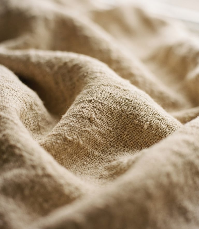 Intimate close-up of draped raw linen fabric in warm sand tones, soft diffused daylight, shallow depth of field, 35mm film