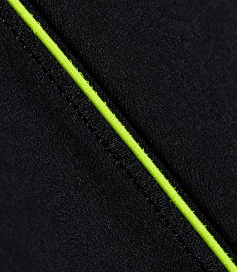 Macro close-up of high-tension flatlock stitching on black moisture-wicking athletic fabric, neon volt thread details, dramatic studio side lighting showing fabric texture