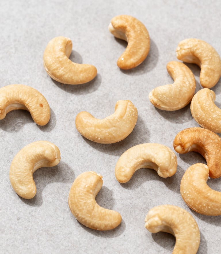 Overhead flat-lay of sorted premium whole cashew nuts on a clean, light-grey stone surface, bright natural daylight, sharp focus