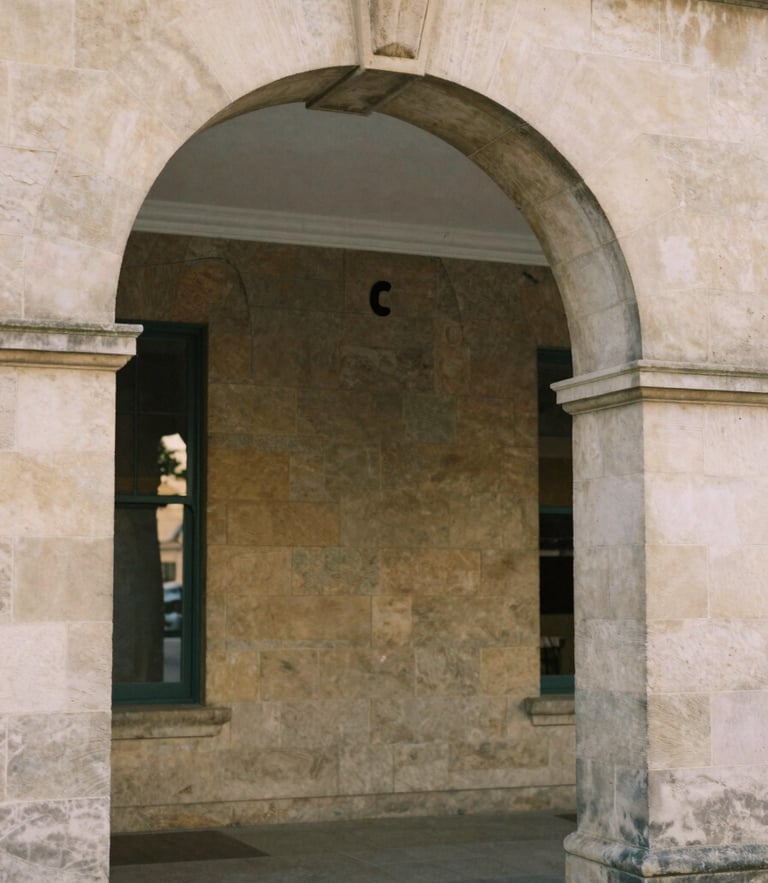 Soft natural daylight reflecting on the stone archway of a historic community center, warm editorial photography, muted earth tones.