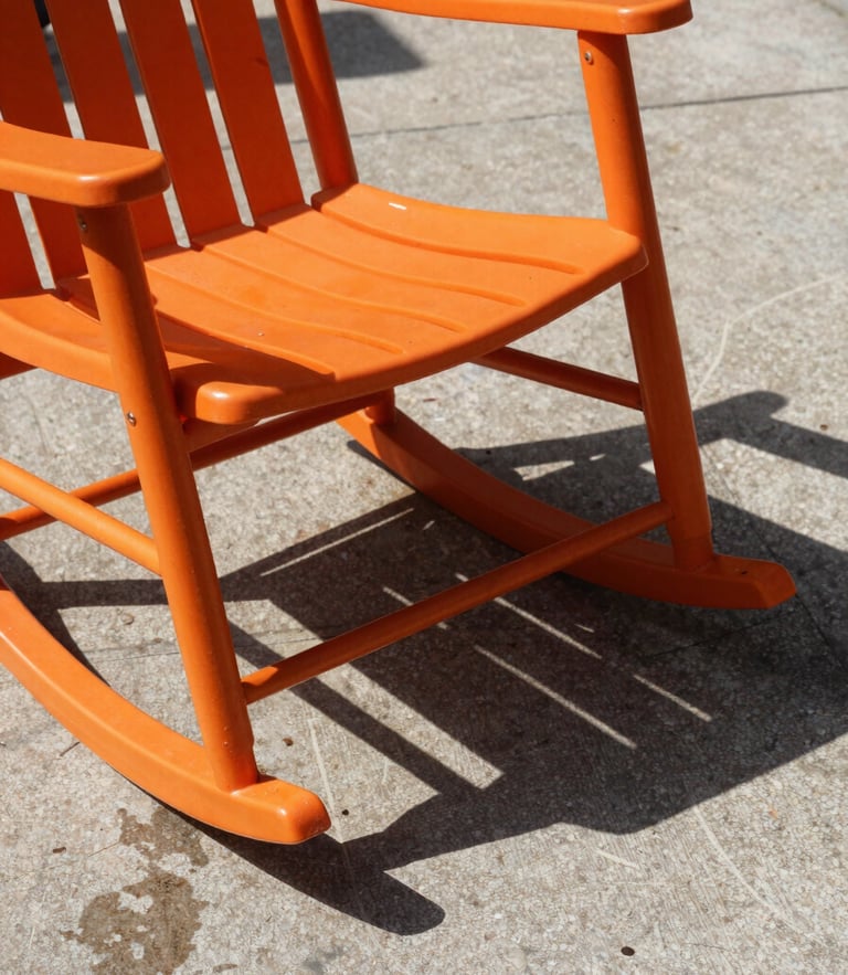 A single orange resin rocking chair casting a sharp, graphic shadow on a wet concrete patio under direct sunlight, texture-focused close-up